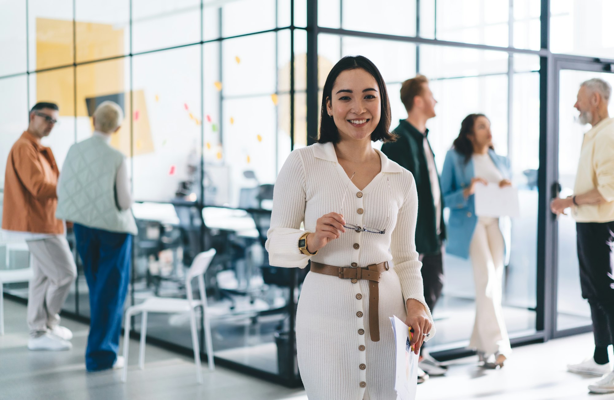 happy young businesswoman with paperwork and eyeglasses posing indoors