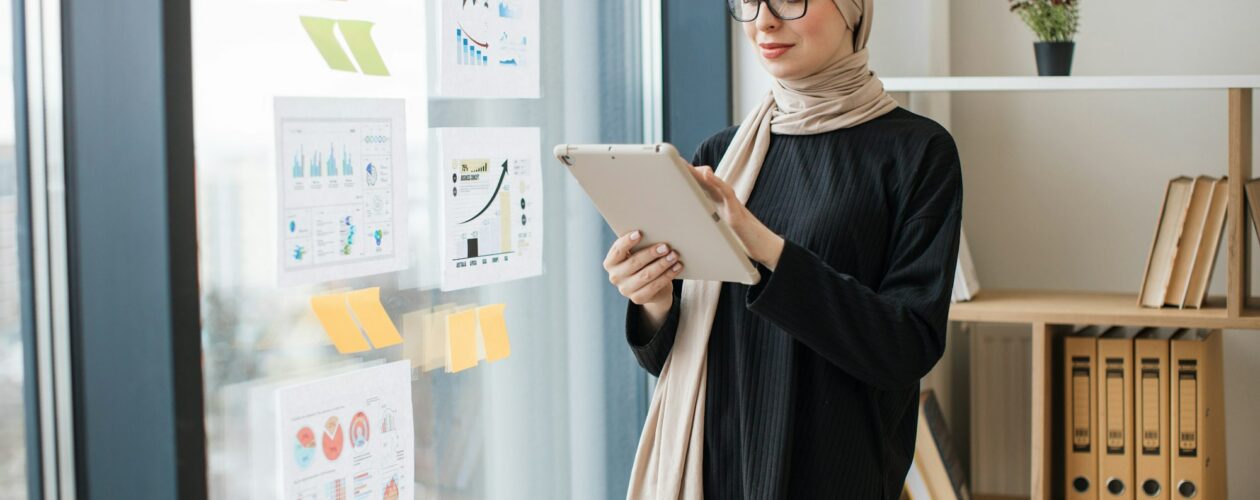 Manager with tablet standing near window with infographics